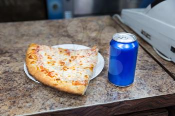 Pizza slice and bank of soda on a counter.