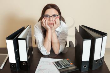 Young female bookkeeper sitting between documents folders in office