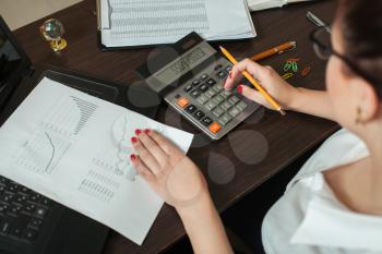 Young female accountant considers on the calculator, top view.