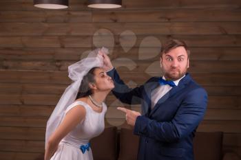 Bride in white dress and veil against surprised groom in suit and bow tie, wooden background