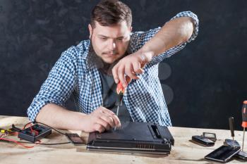 Male service engineer disassembling laptop with screwdriver. Electronic devices repairing technology