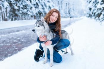 Woman hugs with siberian husky, friendship forever, snowy forest on background. Cute girl walk in park with charming dog
