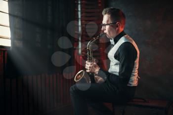 Male saxophonist playing jazz melody on saxophone against the window