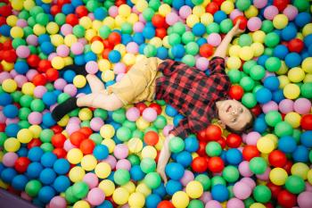 Little boy lying in a pile of colorful inflatable balloons in childrens entertainment center. Happy childhood