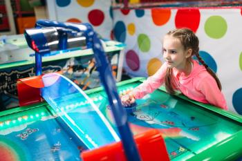 Young girl plays air hockey in entertainment center. Happy childhood. Sport game attraction