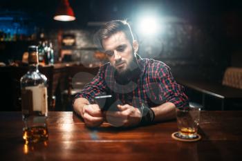 Smiling man sitting at the bar counter and using his phone, relaxation with alcohol. Happy guy having fun, leisure in pub