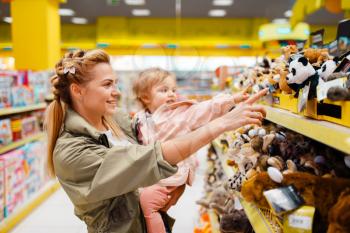 Mother with her little girl choosing toys in kids store. Mom and child in supermarket together, family shopping