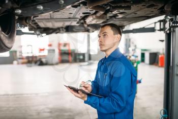 Technician with notebook fills the check list, car on the lift, fixing the problems. Automobile service, vehicle maintenance