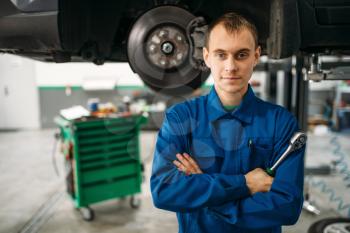 Repairman with wrench against a car on the lift, suspension diagnostic. Automobile service, vehicle maintenance
