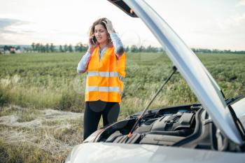 Young girl with phone calls to emergency service, broken car. Trouble with vehicle on road in summer day. Woman in reflecting vest