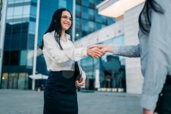 Business woman in glasses and white blouse,  handshake with partner outdoor. Modern building, financial center. Successful female businessperson