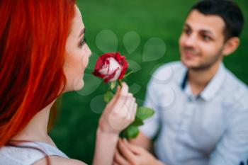 Young man gives flower to beautiful woman, romantic meeting of couple on a bench in summer park