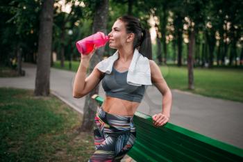 Slim woman poses with sport bottle in summer park. Woman drink water on morning fit workout