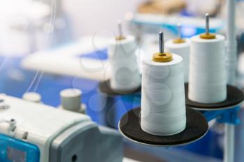 Spools of white threads on sewing machine, closeup. Cloth factory, weaving, textile production, clothing industry