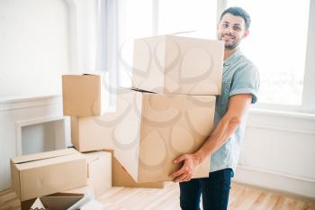 Smiling young man holds cardboard boxes in hands, housewarming. Moving to new house