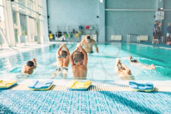 Kids trying to dive in swimming pool like a trainer. Instructor shows an exercise how to dive. Healthy sports activity in pool. Sportive kids activity in modern sport center with pool, clean blue water.