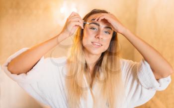 Happy woman in white bathrobe doing makeup in bathroom, facial skincare in bathroom. Bodycare and hygiene, healthcare 