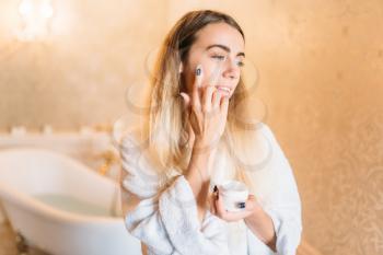 Smiling woman in white bathrobe, facial skincare in bathroom. Bodycare and hygiene, healthcare 