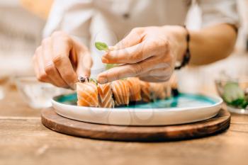 Male person cooking sushi rolls with salmon on wooden table, japanese food preparation process. Traditional asian cuisine, seafood delicious