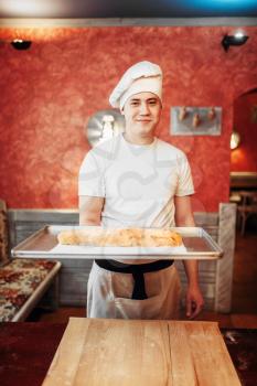 Male chef holds metal baking sheet with classical apple strudel, bakery cooking. Homemade sweet dessert, preparation process