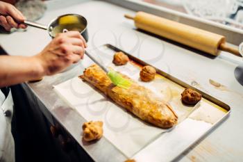 Male chef hand lubricates apple strudel with egg and butter closeup. Homemade sweet dessert cooking, preparation for baking process