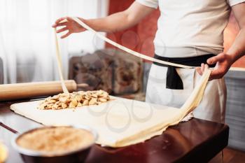 Male chef prepares dough for apple strudel on wooden kitchen table, pastry preparation process. Homemade sweet dessert