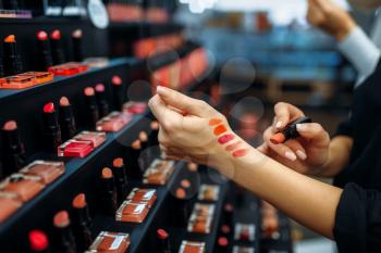 Female customer testing lipstick in the make-up shop. Cosmetics choosing in beauty store, make-up salon