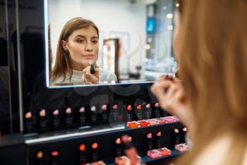 Female customer looks at the mirror in the makeup shop. Nail varnish choosing in beauty store, make-up salon