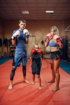 Young family in gloves on kickboxing training, gym interior on background. Couple and little boy on self-defense workout, martial arts practicing