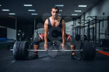 Male powerlifter preparing deadlift a barbell in gym. Weightlifting workout, lifting training, athlete works with weight in sport club