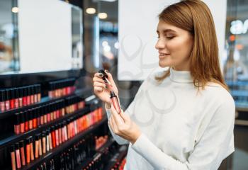 Female customer looks on lip liner in cosmetics store. Woman against showcase in beauty shop
