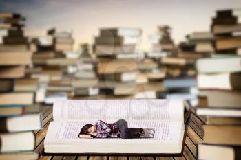 Little young woman sleeping on an open book, scale effect. Knowledge and education, reaiding concept