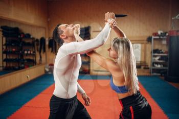 Woman makes punch to the throat, self-defense workout with male personal trainer, gym interior on background. Female person on training, self defense practice