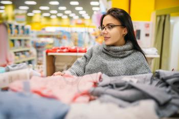 Cheerful future mother in glasses buys childrens clothes in the store for newborns. Pregnant woman in shop of goods for infants