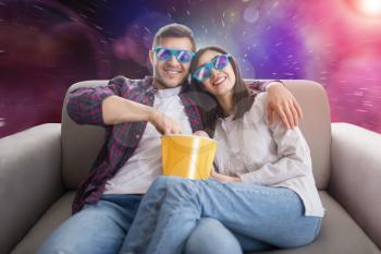 Happy couple in 3D glasses sitting on couch and watch tv, man and woman eats popcorn, magic space on background