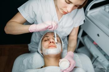 Doctor in gloves rubs the cream on female patient face, cosmetology clinic. Facial skincare, rejuvenation procedure in spa