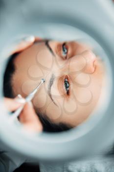 Female patient face, view on through a magnifying glass, cosmetology clinic. Facial skincare in spa salon, health care, beauty medicine