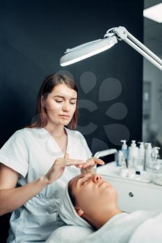 Beautician apply the cream mask to female patient face, cosmetology clinic. Facial skincare, rejuvenation procedure in spa salon, beauty medicine