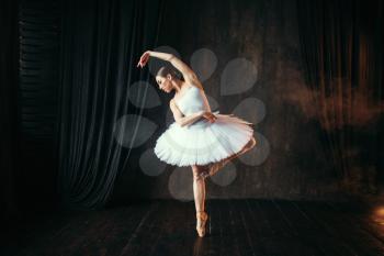 Graceful ballerina in white dress dancing on theatrical stage. Classical ballet dancer training in class
