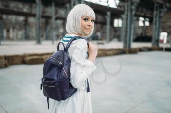Anime style blonde girl with backpack. Cosplay, japanese culture, doll in dress on abandoned factory