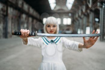 Pretty anime style blonde woman with sword. Cosplay fashion, japanese culture, doll with blade on abandoned factory, cute girl with makeup