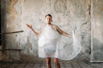 Naked freak man wrapped in packaging film wearing shoes without laces, grunge room interior. Crazy male person in abandoned house