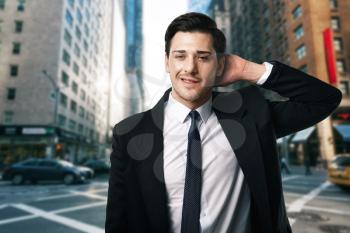 Businessman in tie and black suit poses on the street, business center on background