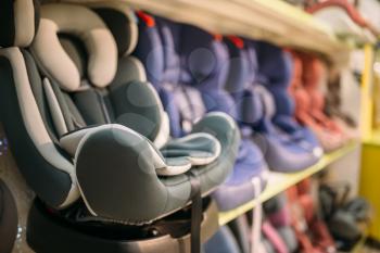 Child car seats variety on shelf in store closeup view, nobody. Goods for safe transportation of children