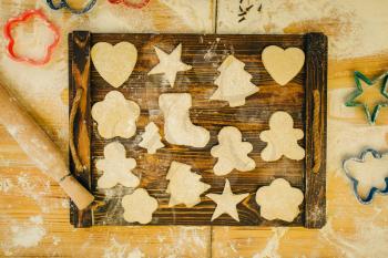 The dough in different forms cuted out by cookie cutters on wooden board, top view, nobody. Hearts, stars and gingerbread man, pastry templates on the table