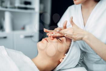 Beautician rubs the cream on female patient face, cosmetology clinic. Facial skincare, rejuvenation procedure in spa salon