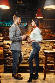 Love couple with alcoholic beverages standing against bar counter, romantic evening. Lovers leisures in pub, husband and wife relaxing together in nightclub