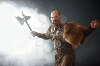 Angry viking with axe, martial spirit, barbarian image. Ancient warrior in smoke on dark background