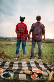 Young couple looking into the distance, picnic in the field. Romantic junket, man and woman on outdoor dinner