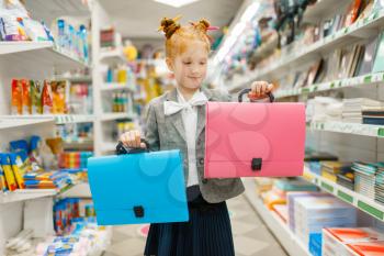 Little school girl with two folders in stationery store. Female child buying office supplies in shop, schoolchild in supermarket